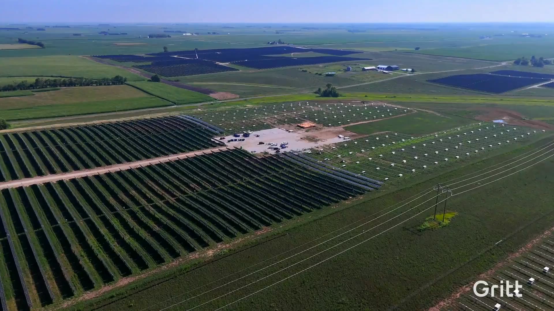 Low aerial down the rows of a large desert solar installation, mounting posts on one side and completed panel rows on the other